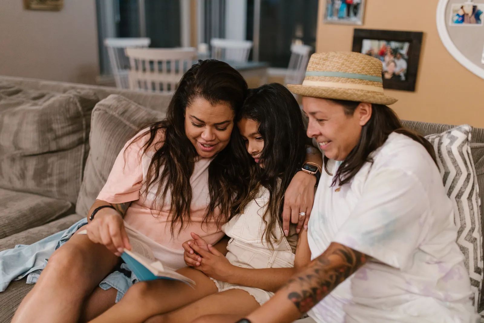 Two women and a girl share a book and a laugh on a sofa at home.